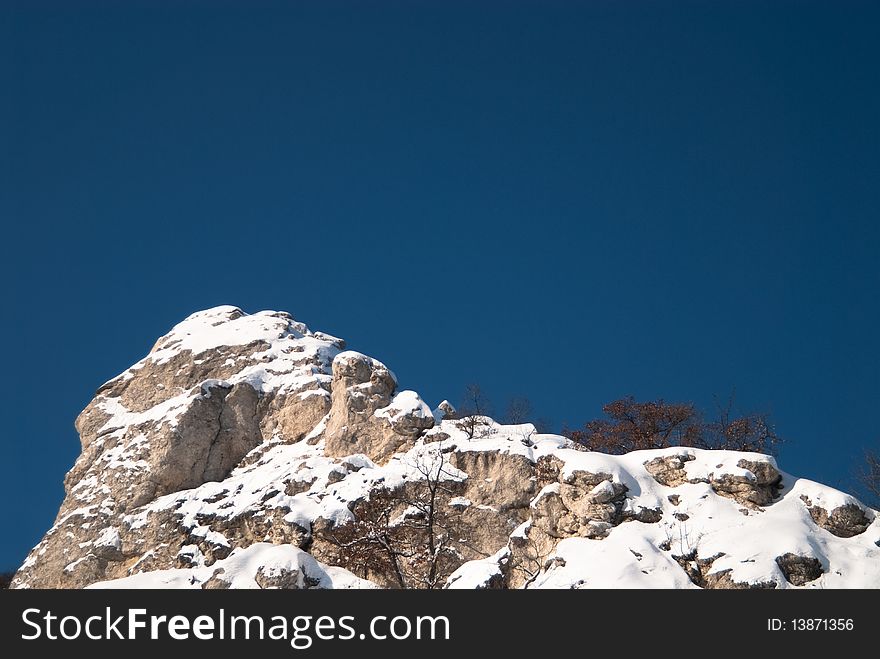 Snow-covered high rocky cliff against clear blue sky, with copy space