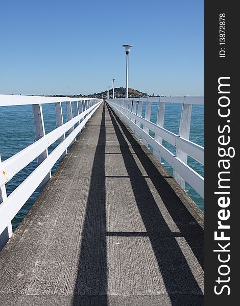 Long jetty with white wooden rails extends into Auckland Harbour. Long jetty with white wooden rails extends into Auckland Harbour