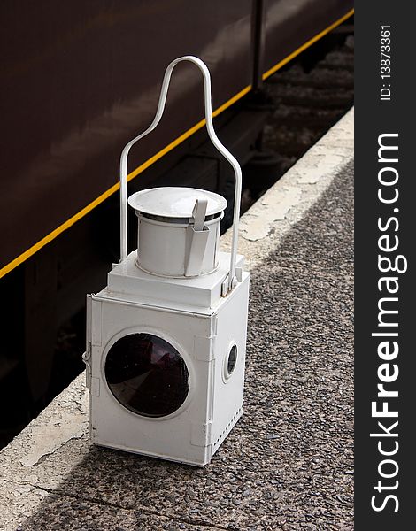 A White railway lamp with red lens resting on the platform