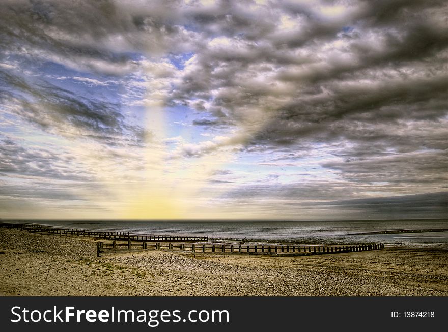 A deserted beach at sunset with a cloudy sky.