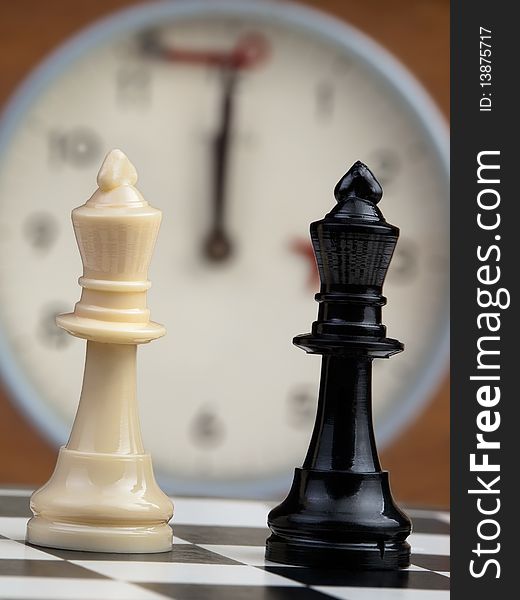 White and black king on the chessboard opposing each other,old chess clock in the background,can be used as concept for conflict,meeting,agreement. White and black king on the chessboard opposing each other,old chess clock in the background,can be used as concept for conflict,meeting,agreement..