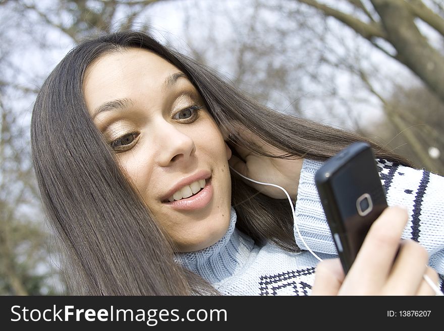 Beautiful girl in a park listening to music from your mobile phone