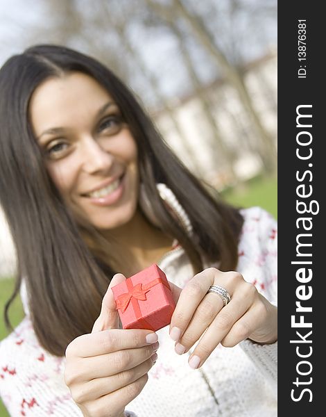 Young woman sitting on a bench in the park and holds a red gift box. Young woman sitting on a bench in the park and holds a red gift box