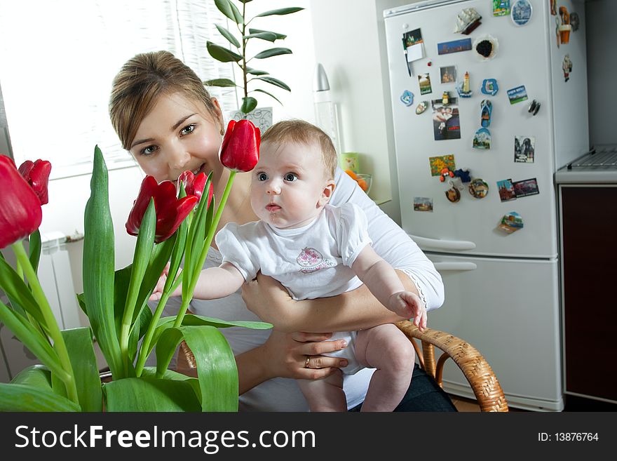 Young beautiful mother feeding her litlle cute baby daughter at the kitchen. Young beautiful mother feeding her litlle cute baby daughter at the kitchen