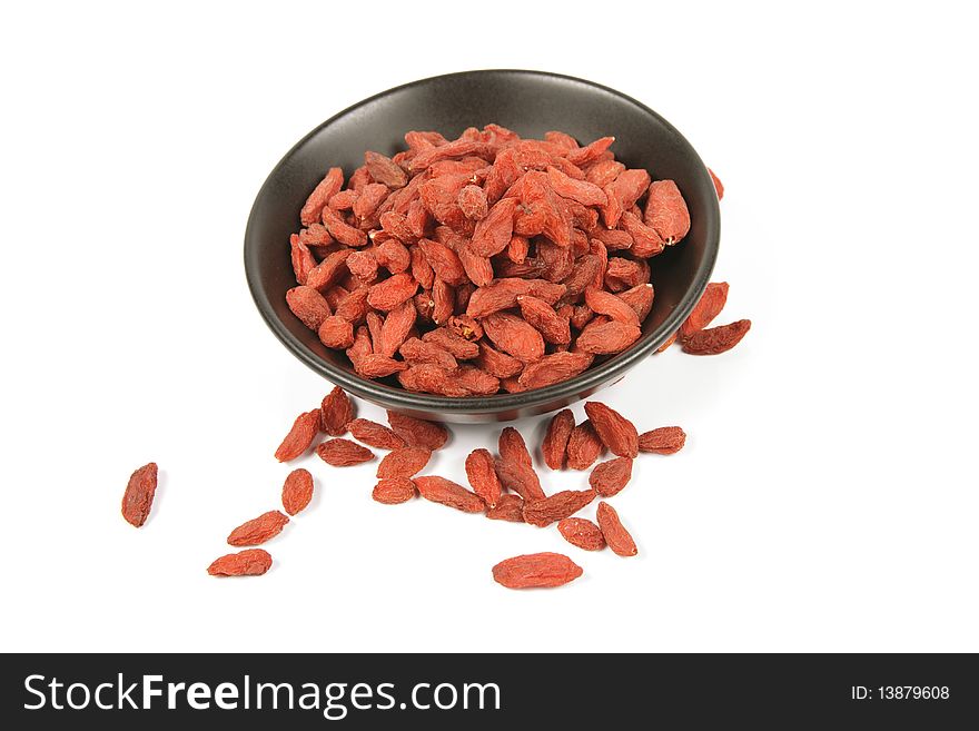 Red dry goji berries in a small black dish on a reflective white background. Red dry goji berries in a small black dish on a reflective white background