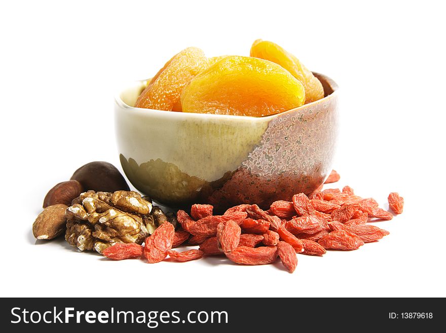 Dried juicy orange apricots in a green and brown bowl with mixed nuts and goji berries on a reflective white background. Dried juicy orange apricots in a green and brown bowl with mixed nuts and goji berries on a reflective white background