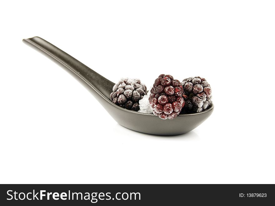 Ripe frozen blackberries on a small black spoon with a reflective white background. Ripe frozen blackberries on a small black spoon with a reflective white background