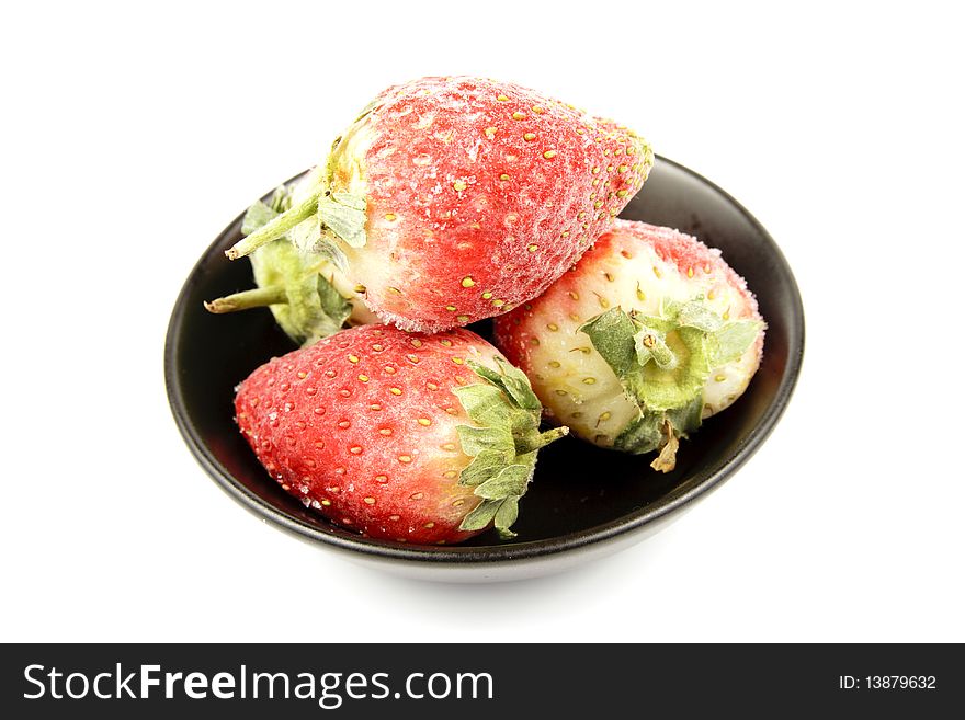 Red ripe frozen strawberries in a small black bowl on a reflective white background. Red ripe frozen strawberries in a small black bowl on a reflective white background