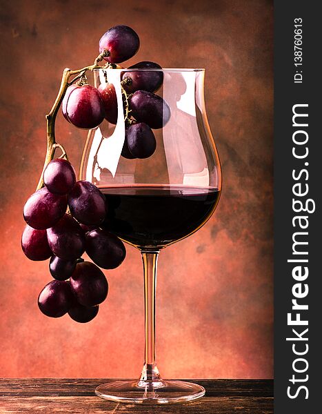 Still life. Closeup of a glass with red wine and bunch of grapes on rough wooden table and dark background. Still life. Closeup of a glass with red wine and bunch of grapes on rough wooden table and dark background