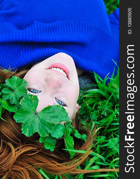 Face and shoulders of redheaded girl laying on the green grass with crown from leaves. Face and shoulders of redheaded girl laying on the green grass with crown from leaves