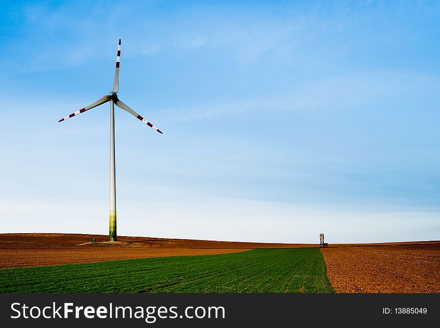 Windmill standing alone on flat cultivated farmland and against a vast blue sky. Horizontal shot. Windmill standing alone on flat cultivated farmland and against a vast blue sky. Horizontal shot.