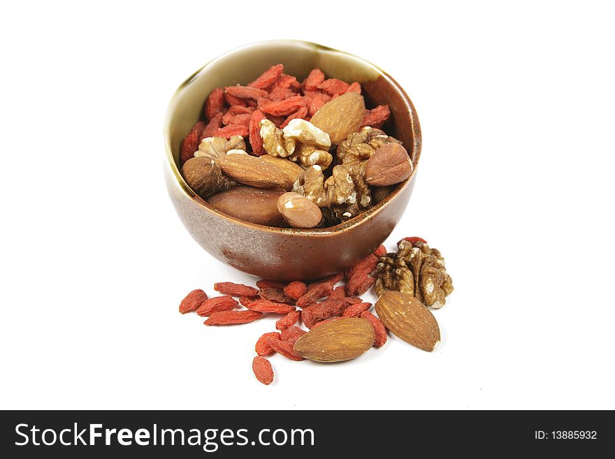 Red dry goji berries with mixed nuts in a green and brown bowl with on a reflective white background. Red dry goji berries with mixed nuts in a green and brown bowl with on a reflective white background