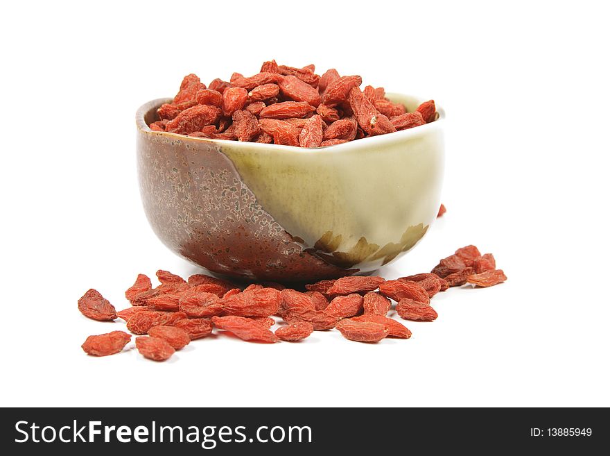 Red dry goji berries in a small green and brown dish on a reflective white background. Red dry goji berries in a small green and brown dish on a reflective white background