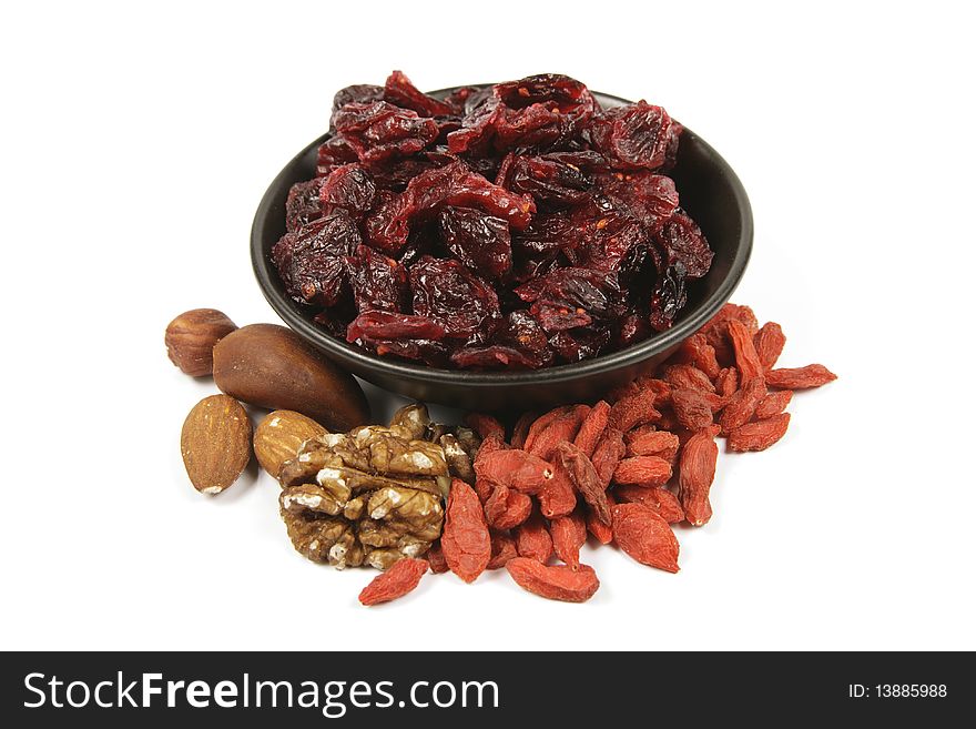 Red ripe dried cranberries in a small black bowl with mixed nuts and goji berries on a reflective white background. Red ripe dried cranberries in a small black bowl with mixed nuts and goji berries on a reflective white background