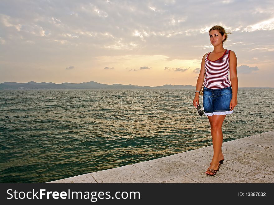 Young fashion model stands in front of sea at sunset. Young fashion model stands in front of sea at sunset.