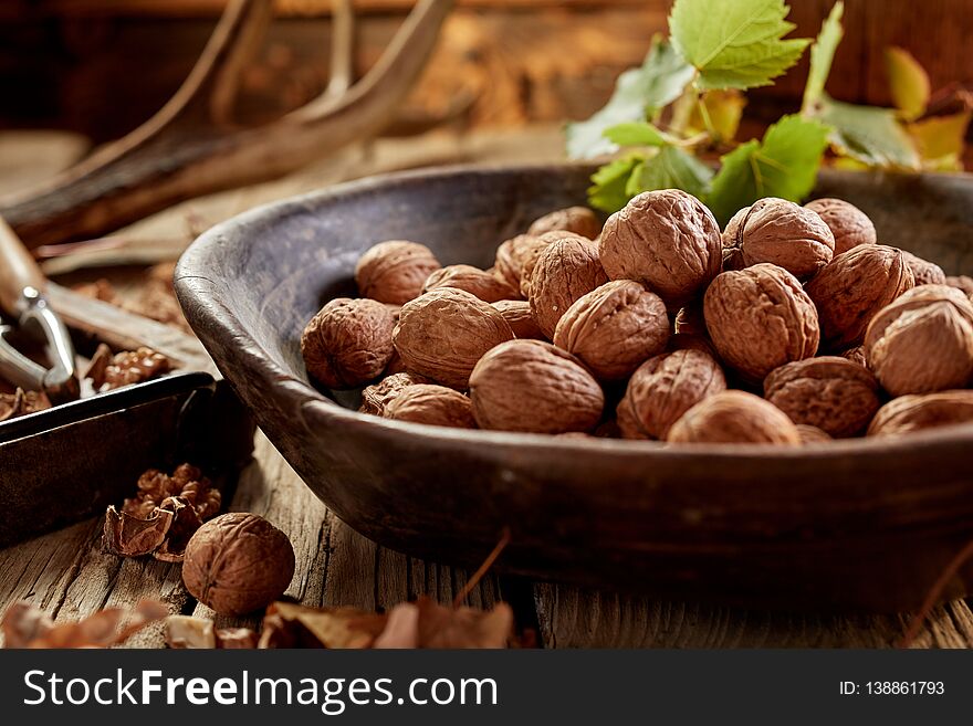 Walnuts in shells in wooden bowl in rustic hunters house on wooden table in close-up. Walnuts in shells in wooden bowl in rustic hunters house on wooden table in close-up