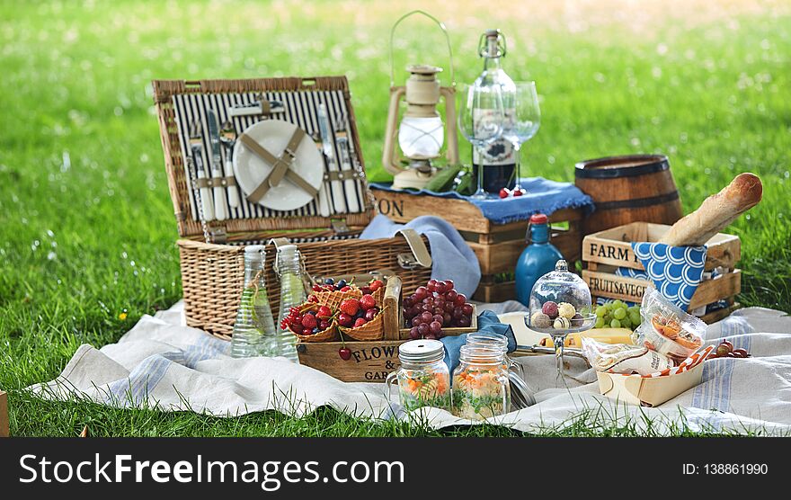 Vintage style picnic hamper with lunch in a park spread out on a rug on the grass with cheese, fresh fruit, bonbons, pickles bread and red wine. Vintage style picnic hamper with lunch in a park spread out on a rug on the grass with cheese, fresh fruit, bonbons, pickles bread and red wine