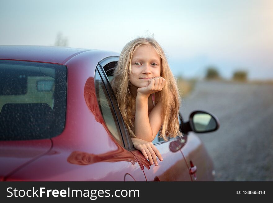 Autotravel with children. happy smiling little girl looking out the car window and sunset at the background