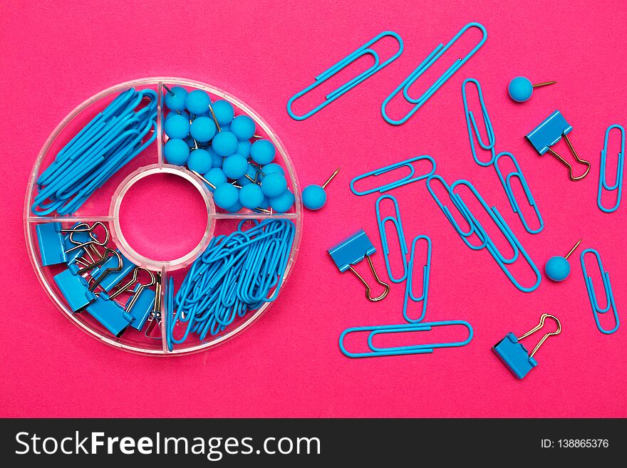 Stationery paper clips, binders and buttons in blue on pink background. Stationery paper clips, binders and buttons in blue on pink background