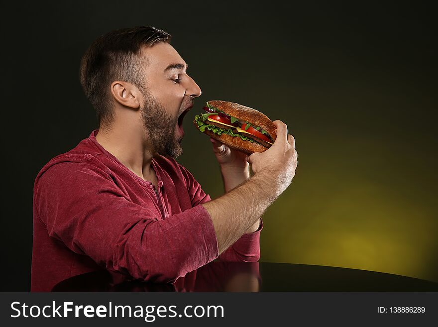 Young man eating tasty burger on color background.