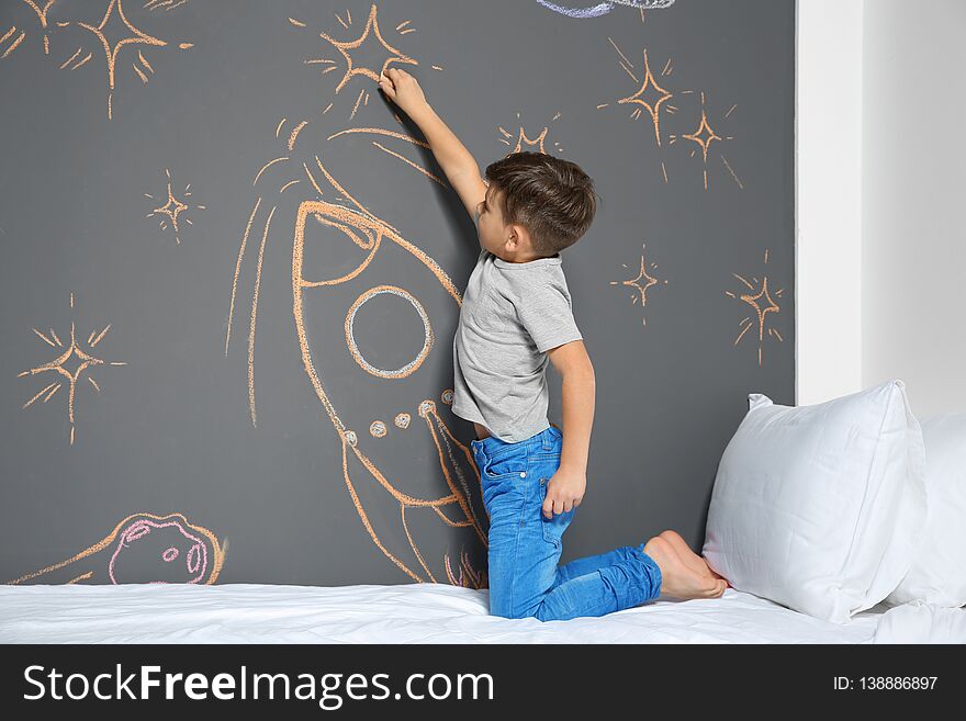 Little child drawing rocket with chalk on wall in bedroom