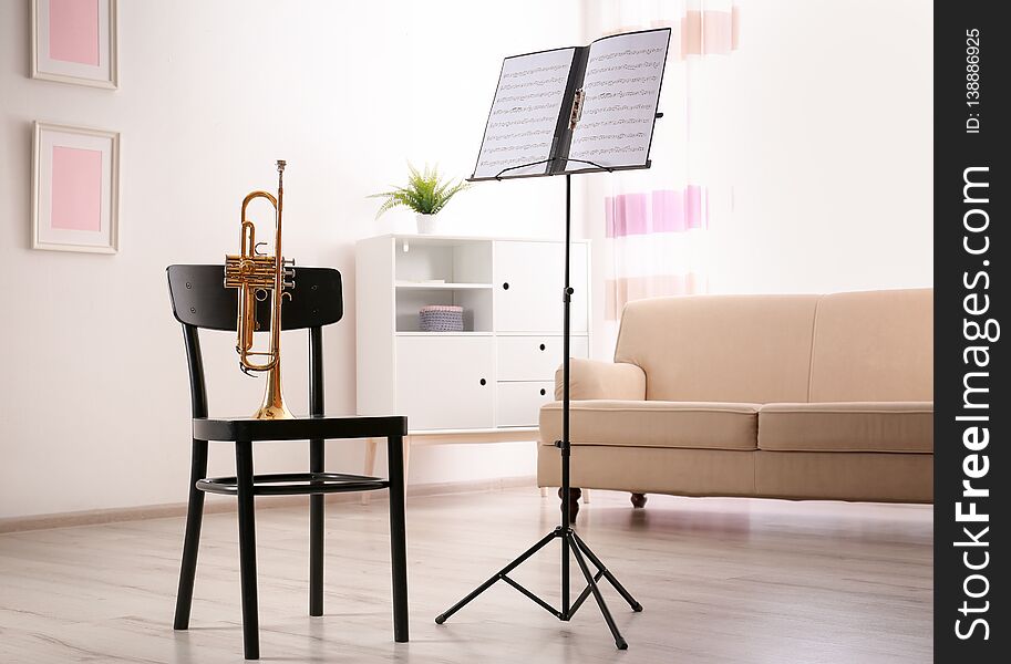 Trumpet, chair and note stand with music sheets in room