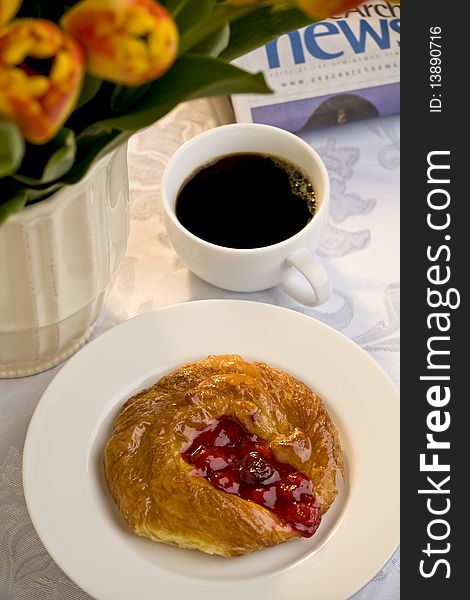 Cherry danish on a white plate with a cup of black coffee, a newspaper and a bunch of tulips. Cherry danish on a white plate with a cup of black coffee, a newspaper and a bunch of tulips
