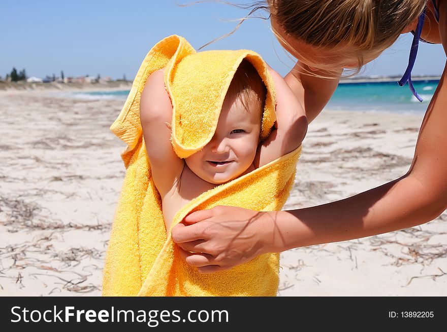 Smiling little girl in a yellow towel on the beach. Caring mother's hands to help her. Smiling little girl in a yellow towel on the beach. Caring mother's hands to help her.