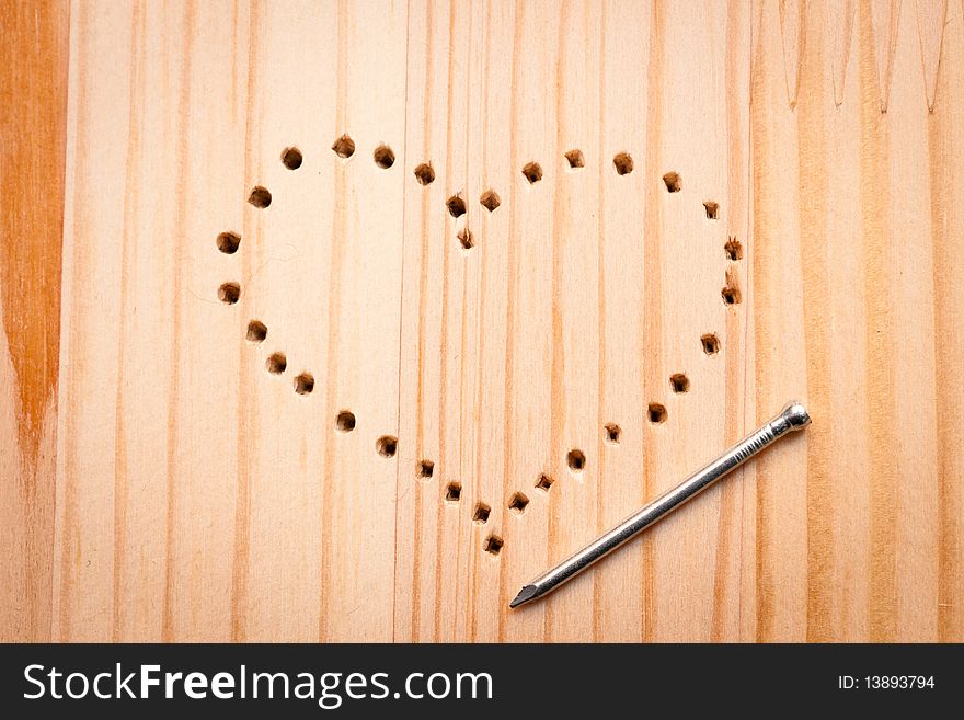 A heart from holes with nail  on wooden desk