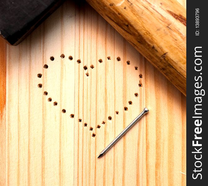 A heart from holes with nail and hummer on wooden desk