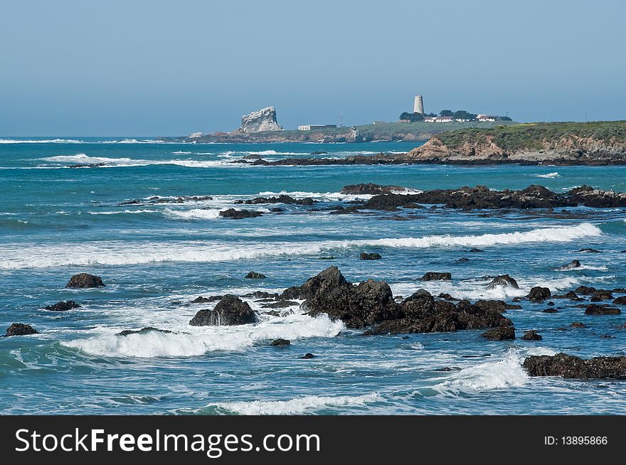 The rocky coastline of California with a lighthouse in the distance. The rocky coastline of California with a lighthouse in the distance