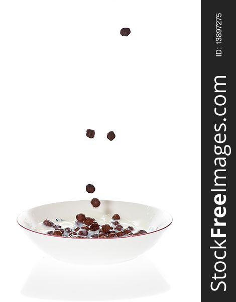 Chocolate cereal falling into a bowl of milk with a white background