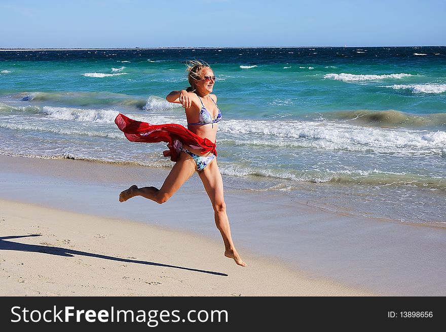 A young girl in a red kerchief runs along the ocean