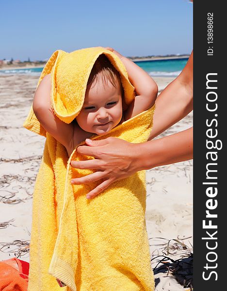 Smiling little girl in a yellow towel on the beach. Caring mother's hands to help her.