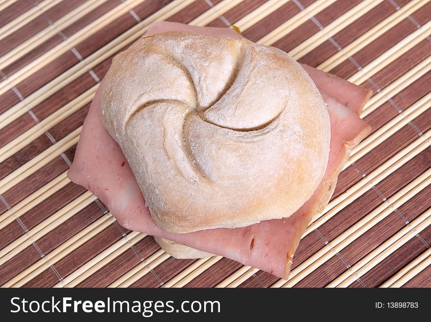 Bread roll filled with Bologna on a bamboo place mat. Bread roll filled with Bologna on a bamboo place mat