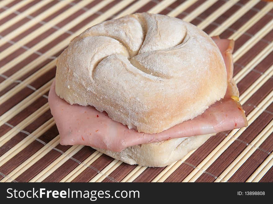 Bread roll filled with Bologna on a bamboo place mat. Bread roll filled with Bologna on a bamboo place mat