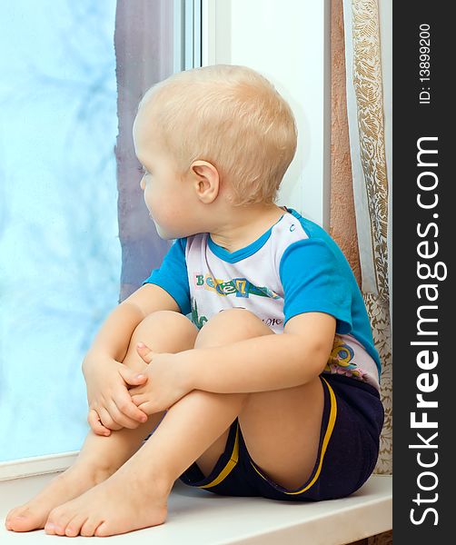 Boy sitting on the windowsill clutching her knees to her, and looks out the window. Boy sitting on the windowsill clutching her knees to her, and looks out the window