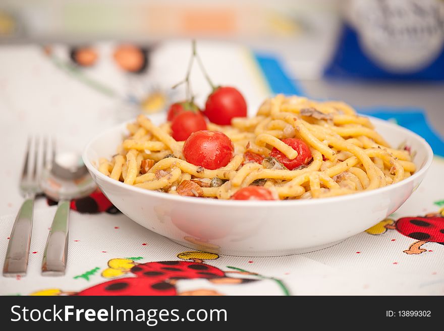 Pasta with cherry tomatoes and anchovies dressing on a plate with fork and spoon near the plate. Shot on a kitchen cloth with shallow depth of field.