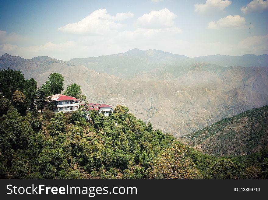 Village in mountain valley in Kashmir, India. Red and white house, blue sky with clouds, mountain range on background. Village in mountain valley in Kashmir, India. Red and white house, blue sky with clouds, mountain range on background.