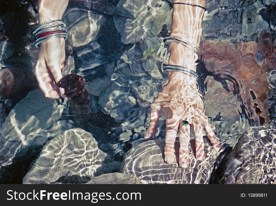Girls hands bangles with under water. Stones and leafes on background. Girls hands bangles with under water. Stones and leafes on background.