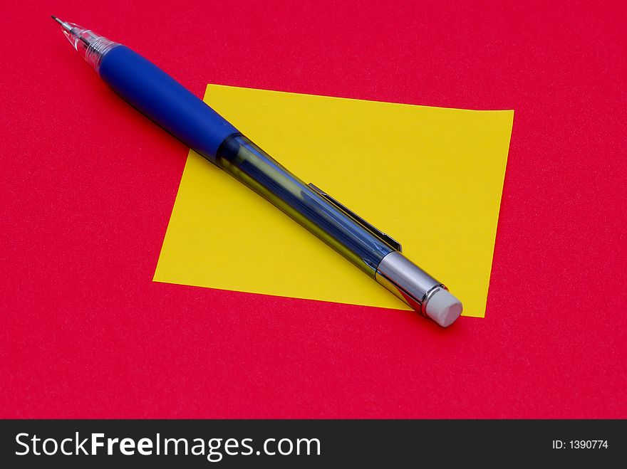 A pencil and a sticky note on a red background. A pencil and a sticky note on a red background