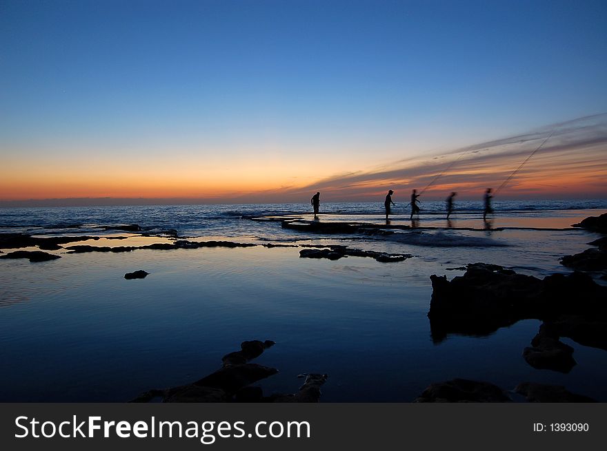 A group of fisherman pictured walking after fishing at the sea side during sunset. A group of fisherman pictured walking after fishing at the sea side during sunset.