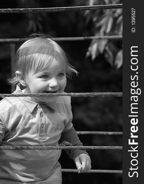 An outdoor portrait of a toddler in black and white peaking through a rail. An outdoor portrait of a toddler in black and white peaking through a rail