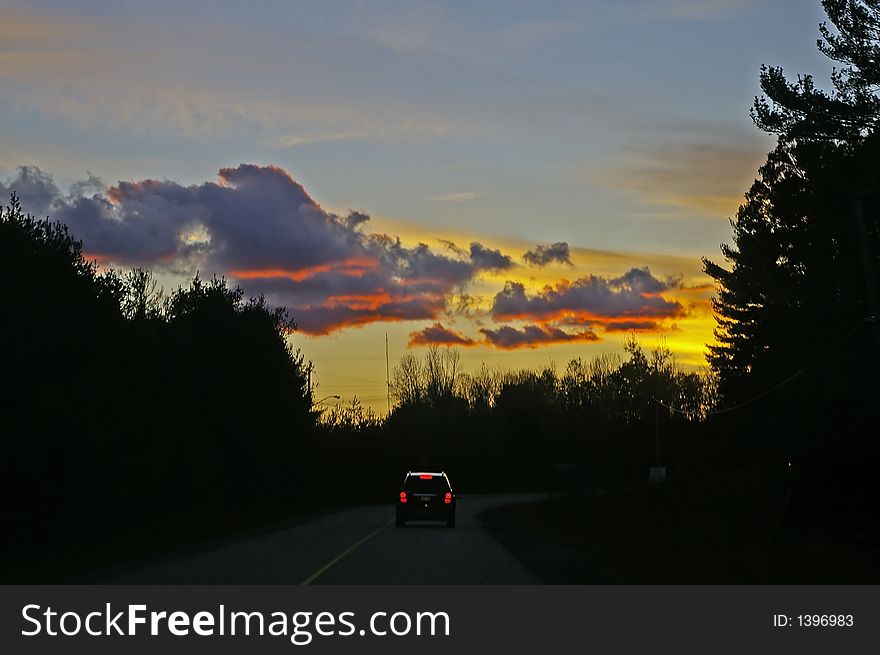 Driving home into a sunset along a two-lane road leaving cottage country.  SUV visible on road in distance. Driving home into a sunset along a two-lane road leaving cottage country.  SUV visible on road in distance.