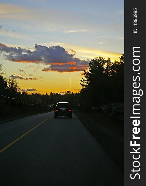 Driving home into a sunset along a two-lane road leaving cottage country.  SUV visible on road in distance. Driving home into a sunset along a two-lane road leaving cottage country.  SUV visible on road in distance.