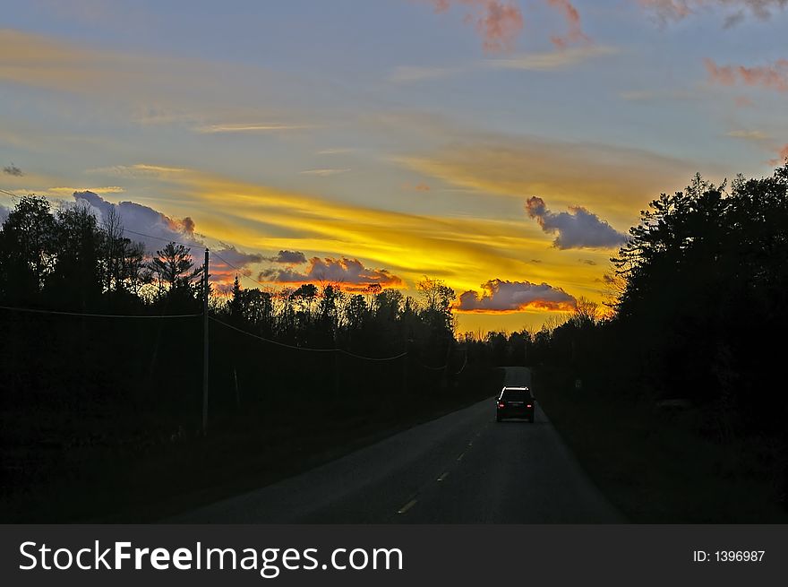 Driving home into a sunset along a two-lane road leaving cottage country.  SUV visible on road in distance. Driving home into a sunset along a two-lane road leaving cottage country.  SUV visible on road in distance.