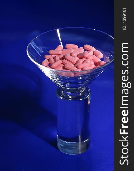 A martini glass filled with pink vitamins on a blue background. A martini glass filled with pink vitamins on a blue background