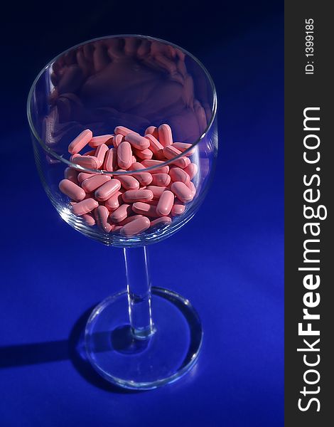 A wine glass pink vitamins on a blue background. A wine glass pink vitamins on a blue background