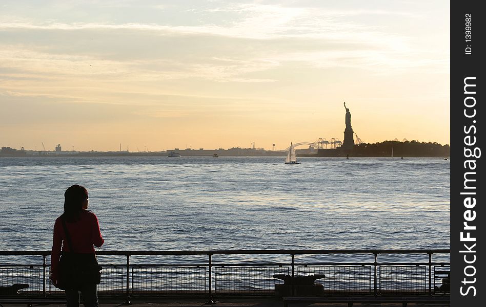 Scenic view from of the Statue of Liberty from Battery Park with young Asian woman looking on. Scenic view from of the Statue of Liberty from Battery Park with young Asian woman looking on