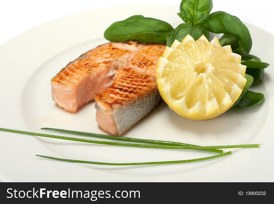 Roasted salmon steak decorated with lemon and basil on plate